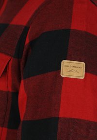 Rood en zwart geruite flanellen blouse met een tan Swedemount-label, met een gestructureerde stof en een klassiek kraagontwerp.