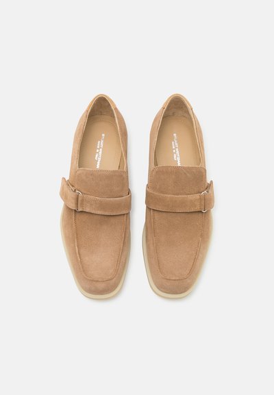 Mocassins en daim marron avec une finition lisse, un bout carré et une sangle sur le dessus. Semelle en caoutchouc de couleur claire. Design simple et élégant.