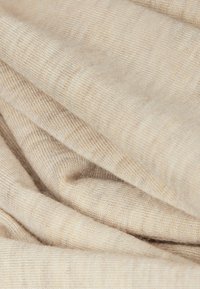 Zachte, lichtbeige stof met een fijne ribbeltextuur en subtiele kleurvariaties, gedrapeerd in losse, vloeiende plooien.