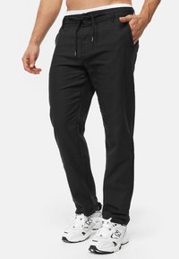 Black utility pants with a medium-weight texture, front pockets, drawstring waist, and a tapered leg design. Paired with white sneakers.