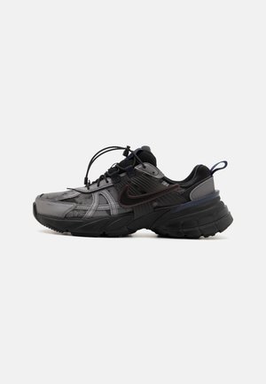 Sort og grå Nike sneaker med tyk sål, trækkrog på hælen og unikt snøresystem med spænde, vist fra siden på hvid baggrund.