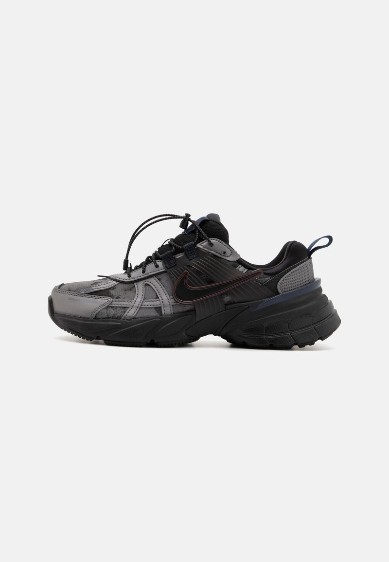 Baskets Nike noires et grises avec semelle épaisse, languette au talon et système de laçage unique à bouton, vues de côté sur fond blanc.