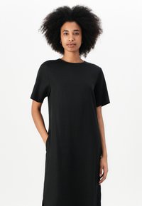 Black dress made of smooth fabric, featuring short sleeves, a round neckline, side pockets, and a straight silhouette with side slits.