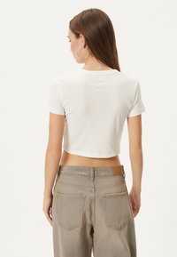 Klippe hvid t-shirt med korte ærmer, blødt stof og rund halsudskæring, parret med højtaljede beige jeans med baglommer.