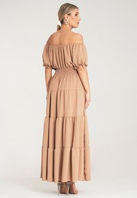 Maxi sukienka w jasnym beżu z dekoltem off-the-shoulder, bufiastymi rękawami, marszczonym pasem i fasonem spódnicy z falbanami. Gładka tekstura tkaniny.