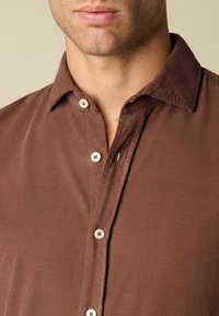 Bruine shirt met kraag, gemaakt van een gestructureerde stof, met knoopsluitingen en een relaxte pasvorm met zichtbare stikseldetails.