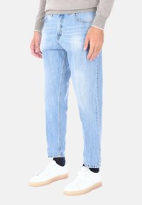 Jeans in denim azzurro chiaro con una vestibilità comoda, presentano dettagli di sbiadimento e un taglio dritto. Abbinati a sneaker bianche e calzini neri.