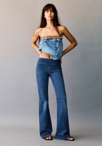 Denim bandeau top met studs riem detail gecombineerd met uitlopende donkerblauwe jeans. Gladde textuur en een gelijkmatige wassing.