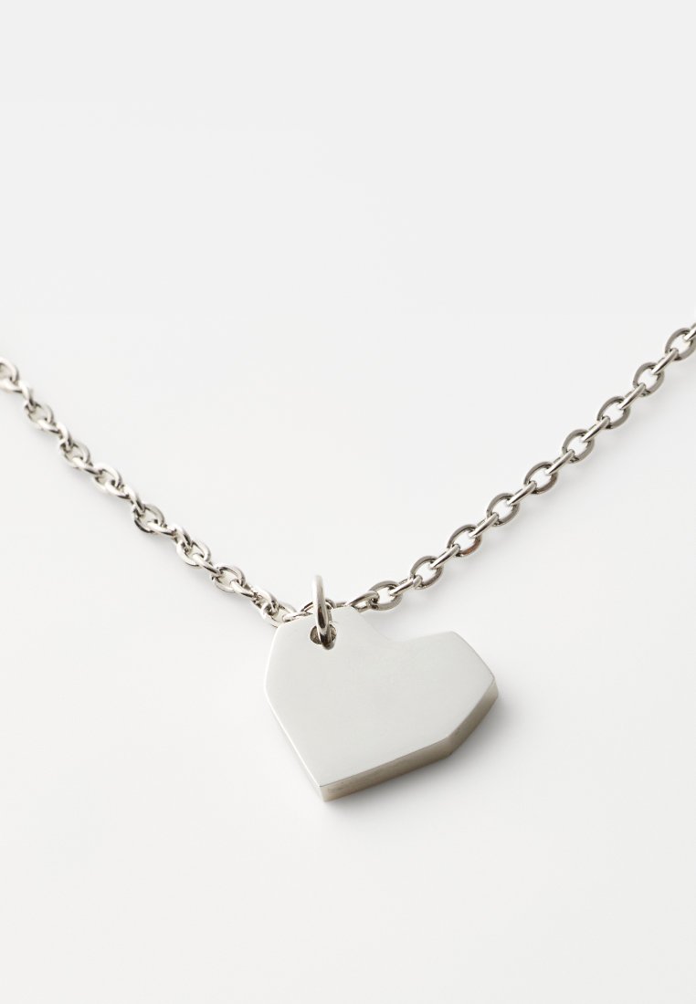 Silbernes Metallkette mit einem flachen, winkligen herzförmigen Anhänger, der von einer verlinkten Kette hängt. Hat eine glatte, reflektierende Oberfläche.