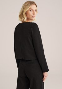 Černý zkrácený blazer s dlouhými rukávy, strukturovaná tkanina a jednoduchý kulatý výstřih. Obsahuje jemný šev na zadní straně, střih přizpůsobený postavě.