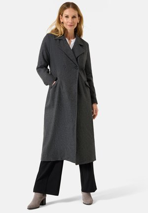 Gray double-breasted wool coat with notched lapels, side pockets, and a long, straight fit. Worn over black pants and gray ankle boots.