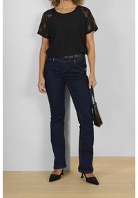 Svart spetskortärmad topp, mörkblå skinny jeans, svart bälte och svarta spetsiga klackar. Inkluderar en liten svart handväska.