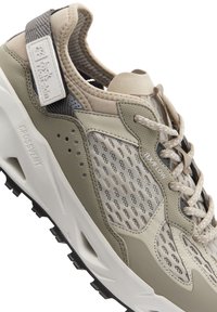 Sneaker leggera con tomaia in rete beige e oliva, dettagli testurizzati, colletto imbottito e suola bianca con trazione nera.