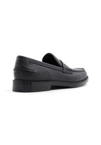 Mocasines de cuero negro con acabado texturado, tacón bajo, punta redondeada y detalle de costura decorativa en la parte superior.
