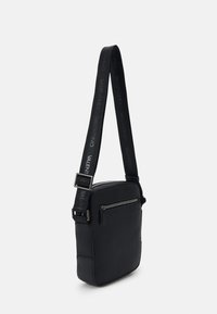 Black crossbody bag made of textured material. Features a zippered front pocket and adjustable strap with logo detail. Rectangular shape.