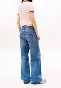 Light pink cropped t-shirt with red trim paired with wide-leg blue denim jeans, featuring a tan leather patch and back pockets.