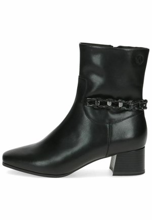 Bottine en cuir noir avec un bout pointu, un talon bloc et une sangle décorative enchaînée autour de la cheville. Texture lisse, design élégant.