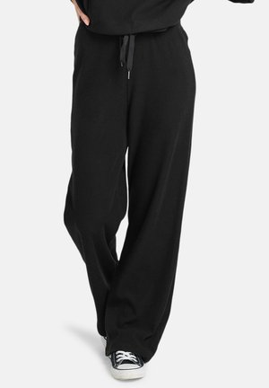 Black ribbed wide-leg pants featuring an elastic waistband with drawstring. Paired with black sneakers. The fabric has a soft texture.