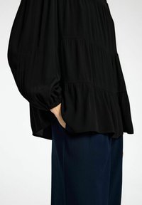 Sort, løstsiddende bluse med lagdelt design og samlede ærmer, lavet af letvægtsstof. Sammen med marineblå bukser.