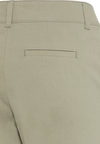 Beige bikses ar gludu tekstūru, ar vienu aizmugures kabatu un jostas cilpiņām, izstrādātas, lai akcentētu figūru.