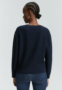 Pull en maille bleu marine avec un motif texturé, des poignets et un ourlet côtelés, et une coupe décontractée, associé à un jean bleu foncé.