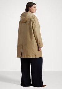 Kaki huva jacka med rak skärning, med vent bak och sidofickor, tillsammans med vida svarta byxor. Slät textur.