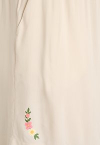 Béžová látka s jemnou textúrou, s kvetinovým vzorom s ružovými a žltými kvetmi na jednej strane. Jednoduchý a čistý dizajn.