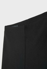 Gros plan sur un tissu noir montrant une section lisse alignée avec la couture, suggérant une partie de la taille ou de la zone supérieure d'un vêtement.