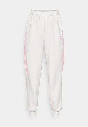 Weißer Jogginghose mit elastischen Bündchen an den Knöcheln, pinken seitlichen Streifen und einem kleinen pinken Adidas-Logo auf der oberen linken Oberschenkel.