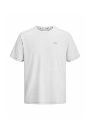 Tiener met krullend haar, die een navy jas, wit T-shirt, navy korte broek, gestreepte witte sokken en witte sneakers draagt, staand en glimlachend.