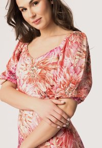 Robe florale rose avec manches bouffantes, présentant un imprimé vibrant de grandes fleurs. Tissu doux avec un décolleté en scoop et des détails de design froncés.