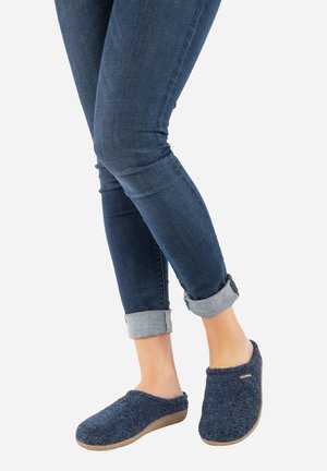 Navy blue woolen clogs with a soft, textured upper and a flexible tan sole, worn with rolled-up dark jeans.