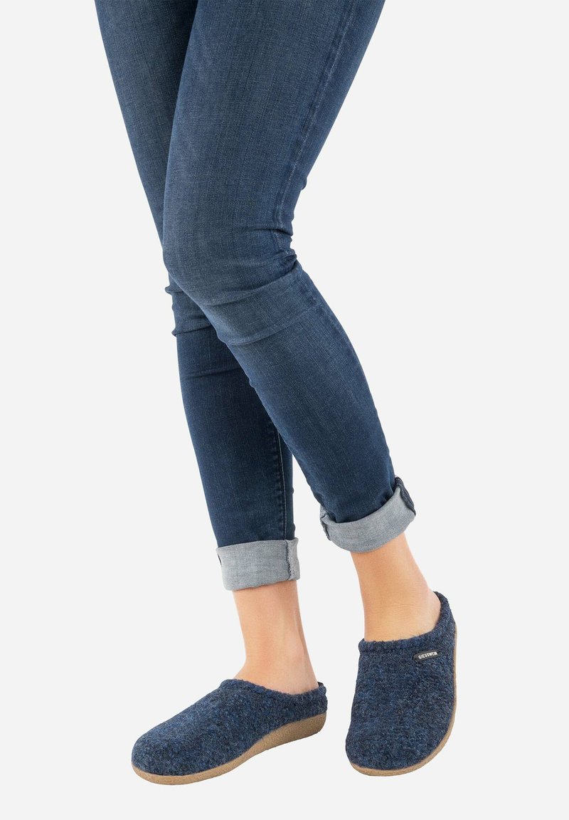Zoccoli in lana blu navy con una parte superiore morbida e strutturata e suola flessibile color cammello, indossati con jeans scuri arrotolati.