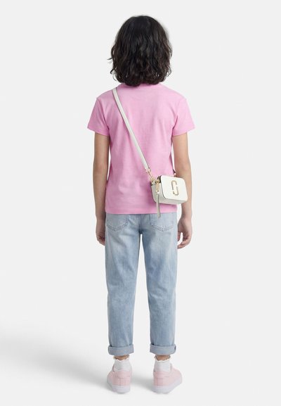 Παιδί με σκούρα μαλλιά μήκους μέχρι τους ώμους, που φοράει ροζ μπλουζάκι, ανοιχτόχρωμο μπλε τζιν, ροζ παπούτσια και λευκή τσάντα χιαστή, γυρισμένο πλάτη.