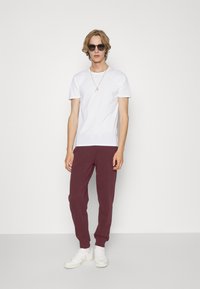 White short-sleeve t-shirt, maroon sweatpants with ribbed cuffs, and white sneakers. Necklace and sunglasses complete the casual look.
