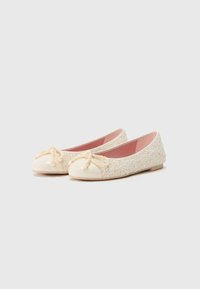 Ballerines avec un bout verni crème, un corps crème texturé et un détail décoratif en corde nouée à l'avant. Doublure rose pâle.