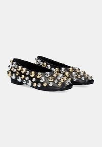 Zapatos planos negros decorados con bolas metálicas en plata y oro de diferentes tamaños, con una textura de cuero suave y tacón bajo.