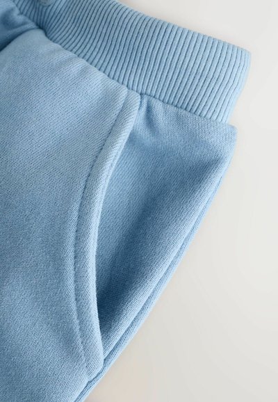 Primer plano de pantalones deportivos de tela de punto azul claro que muestra la cintura elástica acanalada y el detalle de bolsillo lateral.