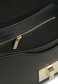 Interno di una borsa a tracolla in pelle nera con una tasca con zip dorata, texture liscia e un dettaglio di chiusura con gancio dorato. Logo BOSS impresso all'interno.
