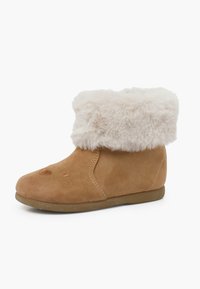 Botines de ante color beige con un suave puño de piel sintética color crema, puntera redondeada, suela plana y detalles de costura mínimas en la parte superior.