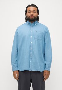 Jasnoniebieska koszula jeansowa z długimi rękawami, kołnierzykiem na guziki, kieszenią na piersi i lekko zaokrąglonym dołem. Miękka w dotyku, o luźnym kroju.