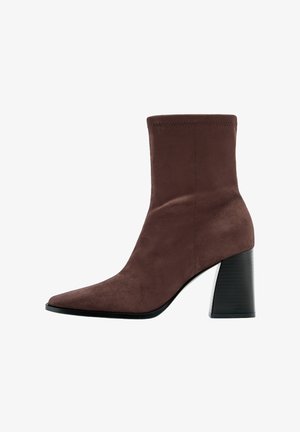 Rjav semiš gležnjar z ostro konico in visokim črnim debelim petom. Ima gladko teksturo in strukturiran dizajn gležnja.