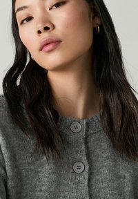 Gray knit sweater with a round neckline, featuring two large gray buttons. Smooth texture and subtle pattern in the fabric.