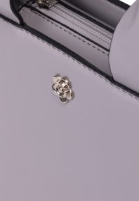 Borsa a mano grigia chiara con una texture liscia, dotata di un'accento metallico floreale e di un compartimento con zip lungo il bordo superiore.