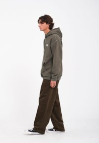 Olijfgroene katoenen hoodie met een voorkantzak en stikdetails, gecombineerd met wijde bruine corduroy broeken en zwarte canvas sneakers.