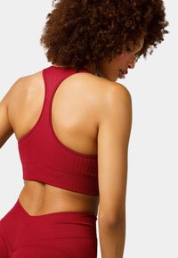 Sostenedor deportivo rojo con diseño de espalda racerback, textura acanalada y costuras en contraste. La tela es elástica, ajustada y diseñada para uso atlético.
