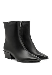 Paire de bottines en cuir noir avec bouts pointus, fermetures éclair latérales et talons blocs bas sur fond blanc.
