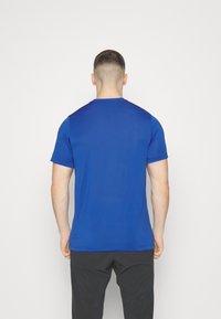 Modré sportovní tričko s kulatým výstřihem a krátkými rukávy. Hladká textura a přiléhavý střih, zobrazeno ze zadní strany na bílém pozadí.
