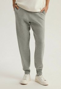 Szare dresy wykonane z miękkiego materiału, z bocznymi kieszeniami, zwężanymi nogawkami i elastycznymi mankietami, zestawione z białymi sneakersami.