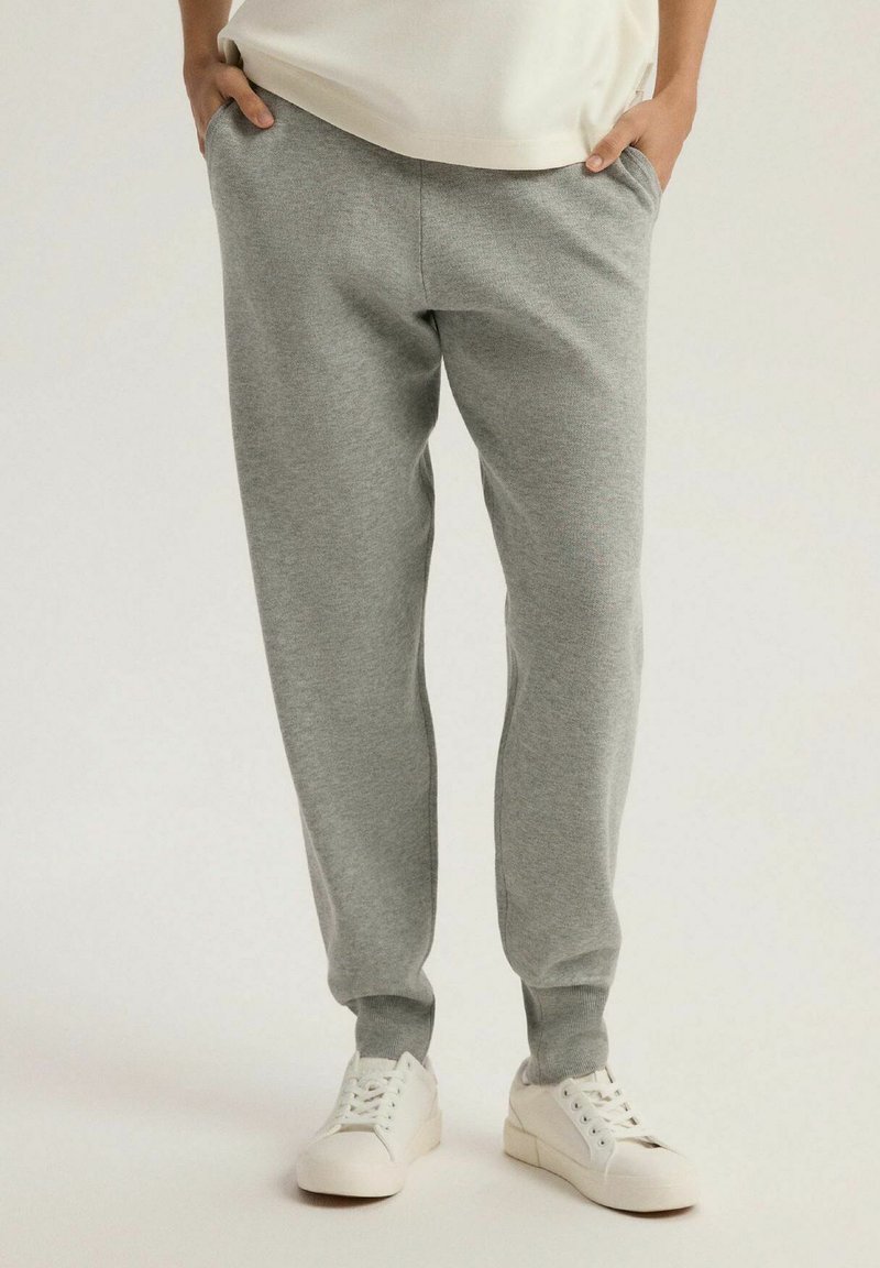 Szare dresy wykonane z miękkiego materiału, z bocznymi kieszeniami, zwężanymi nogawkami i elastycznymi mankietami, zestawione z białymi sneakersami.